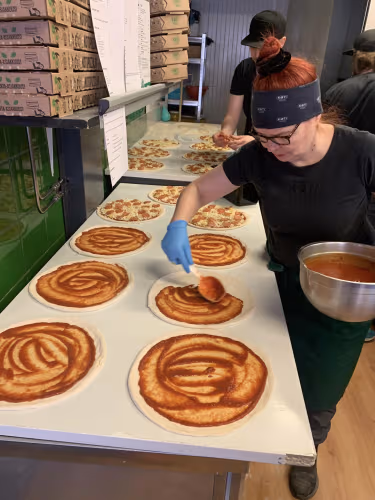 Työntekijä levittämässä tomaattikastiketta pizzapohjille linjastolla