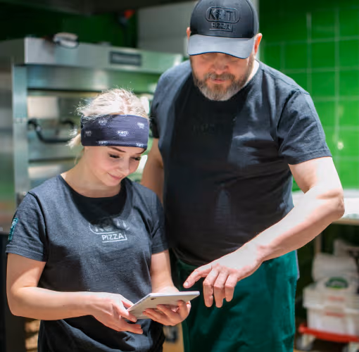 Esihenkilö perehdyttämässä työntekijää tabletin äärellä keittiössä